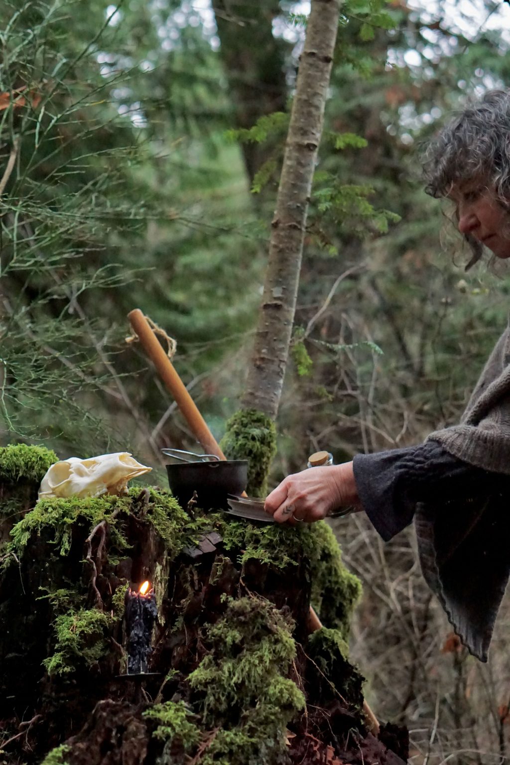 Monika Carless in the forest. There are various mystical items placed in front of her on a hill of moss.